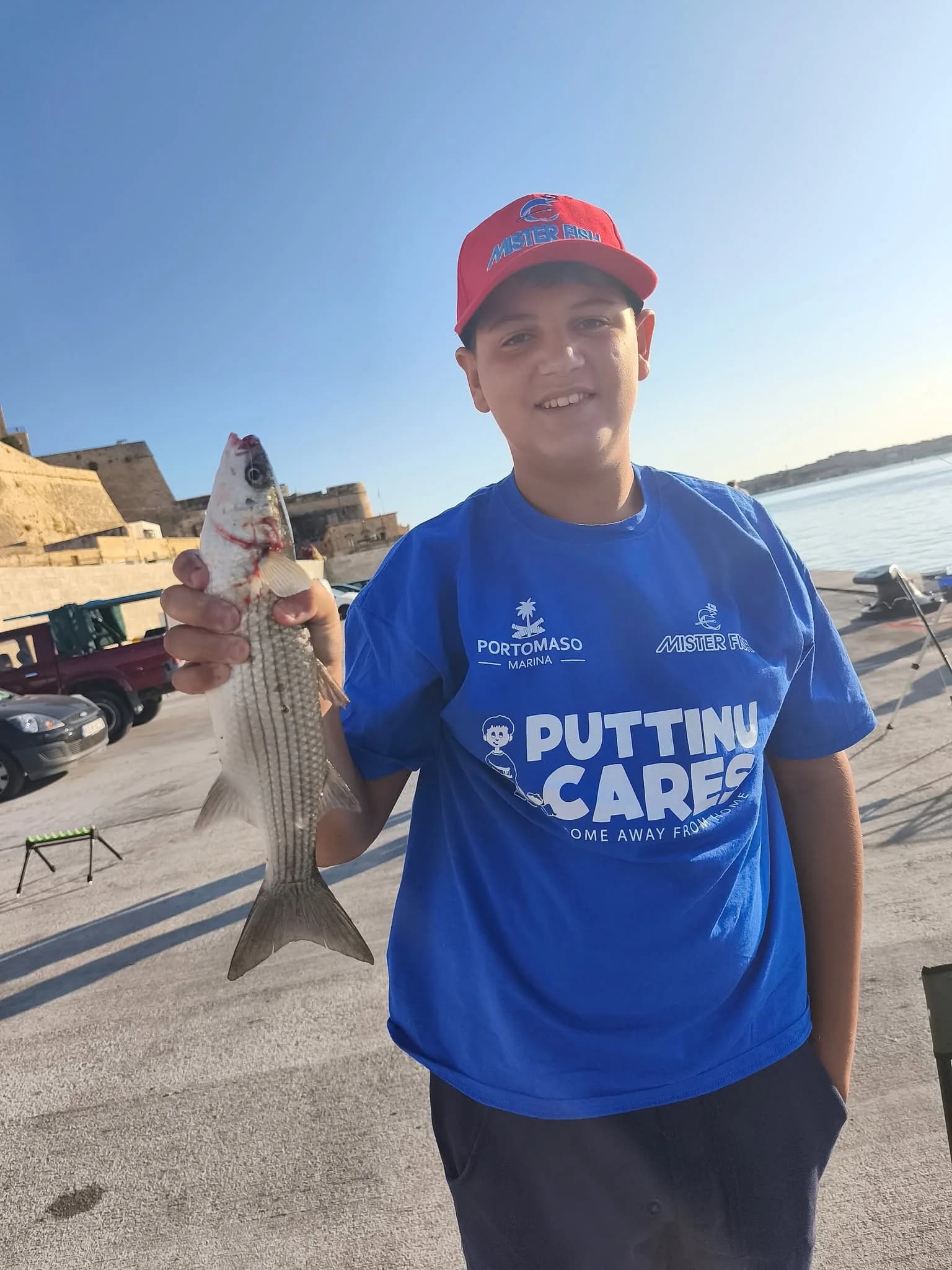 A young angler in a red cap holding a catch beside the water
