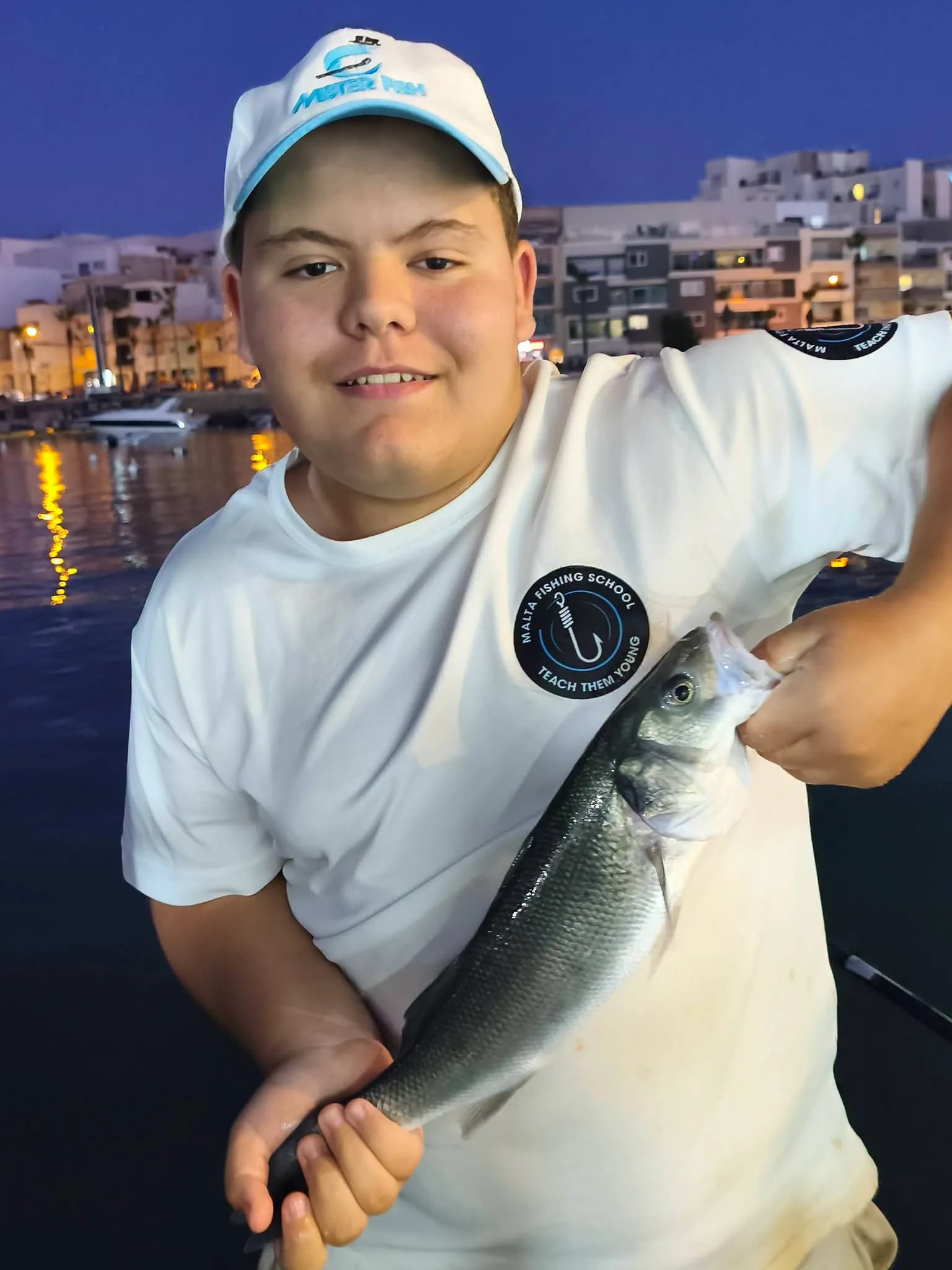 A young angler in a school shirt showing a catch beside the harbour