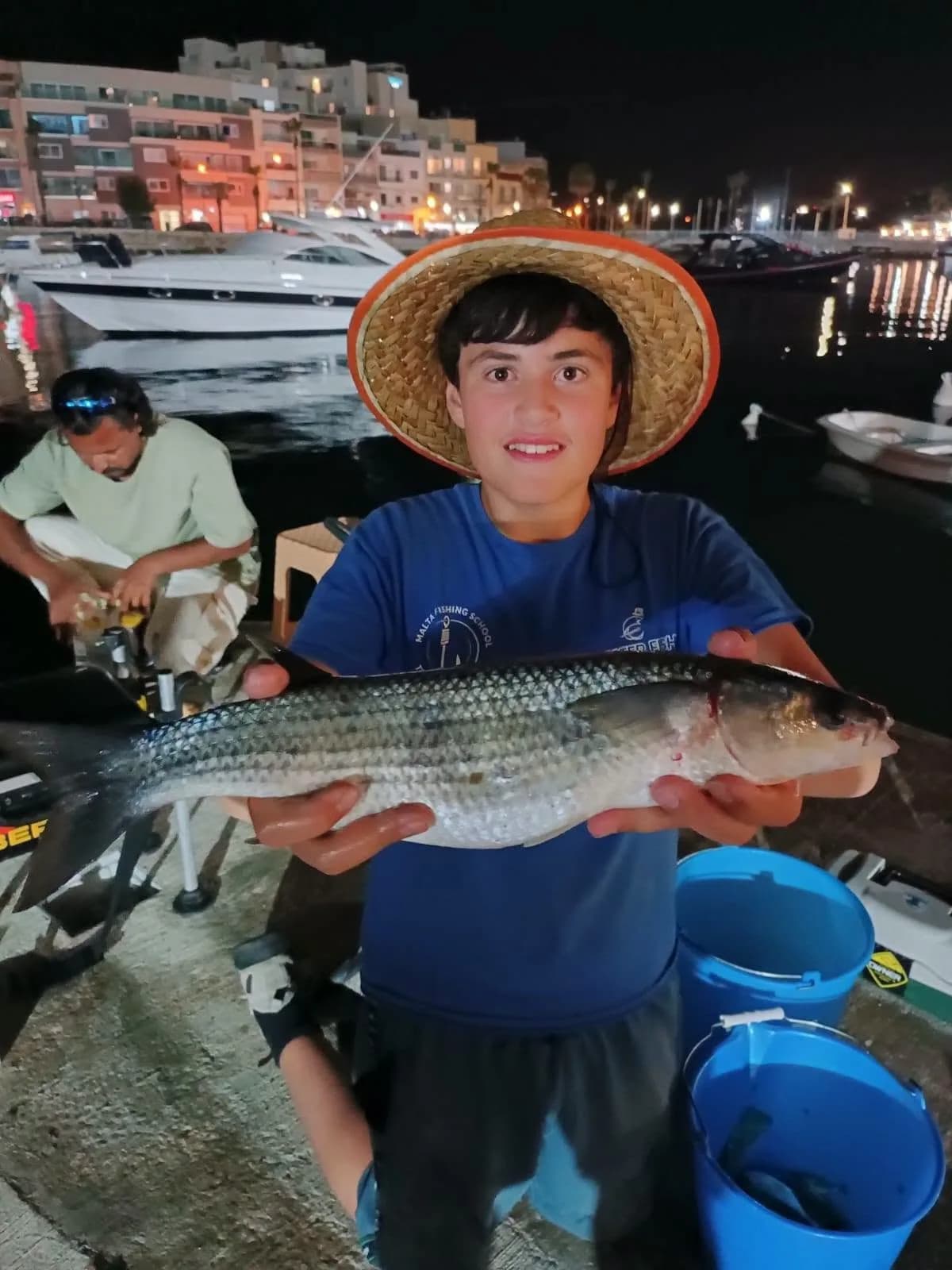 A young angler in a pink cap showing a fish beside the blue sea