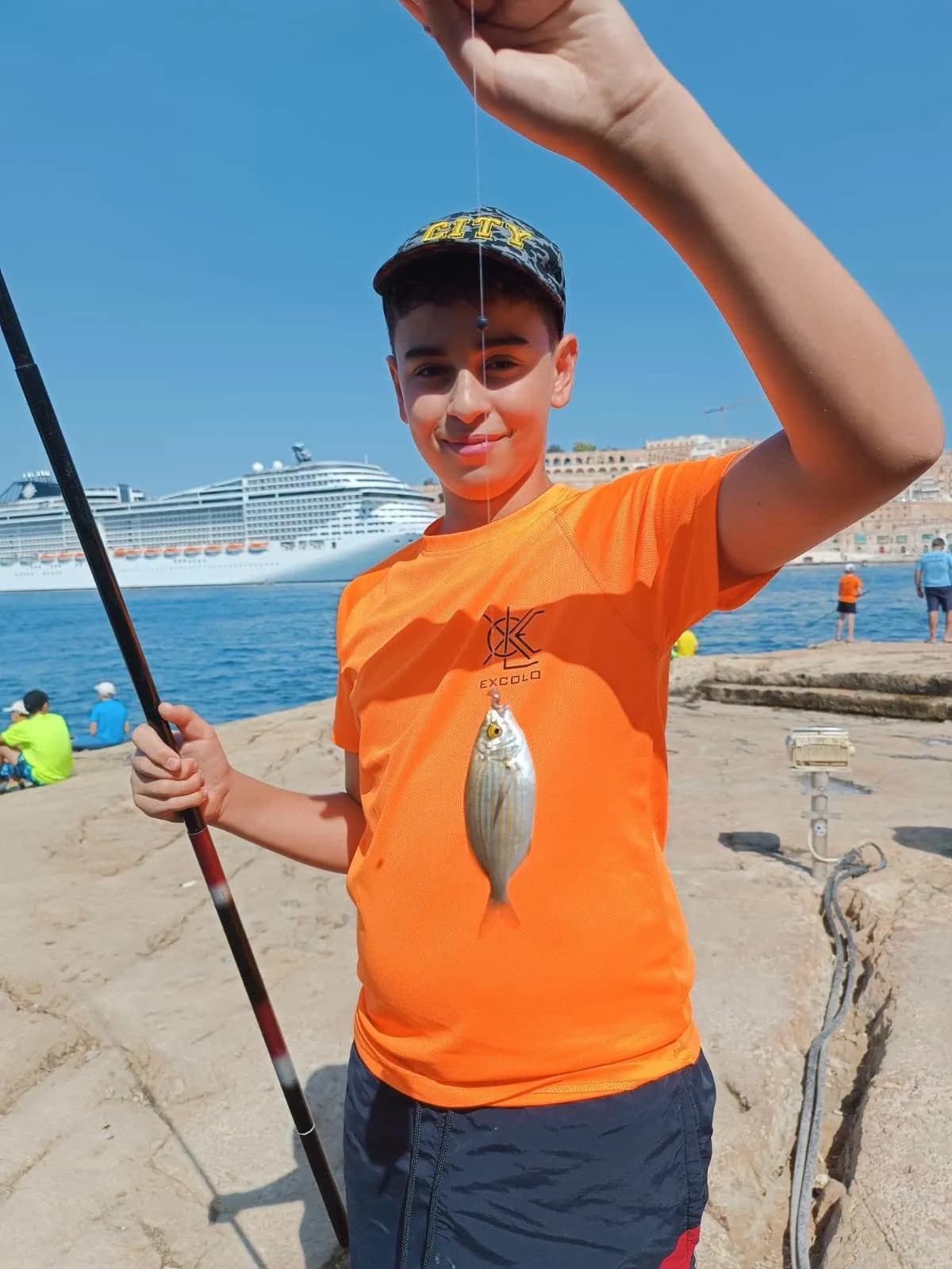 A young angler holding a catch in front of the waterfront buildings