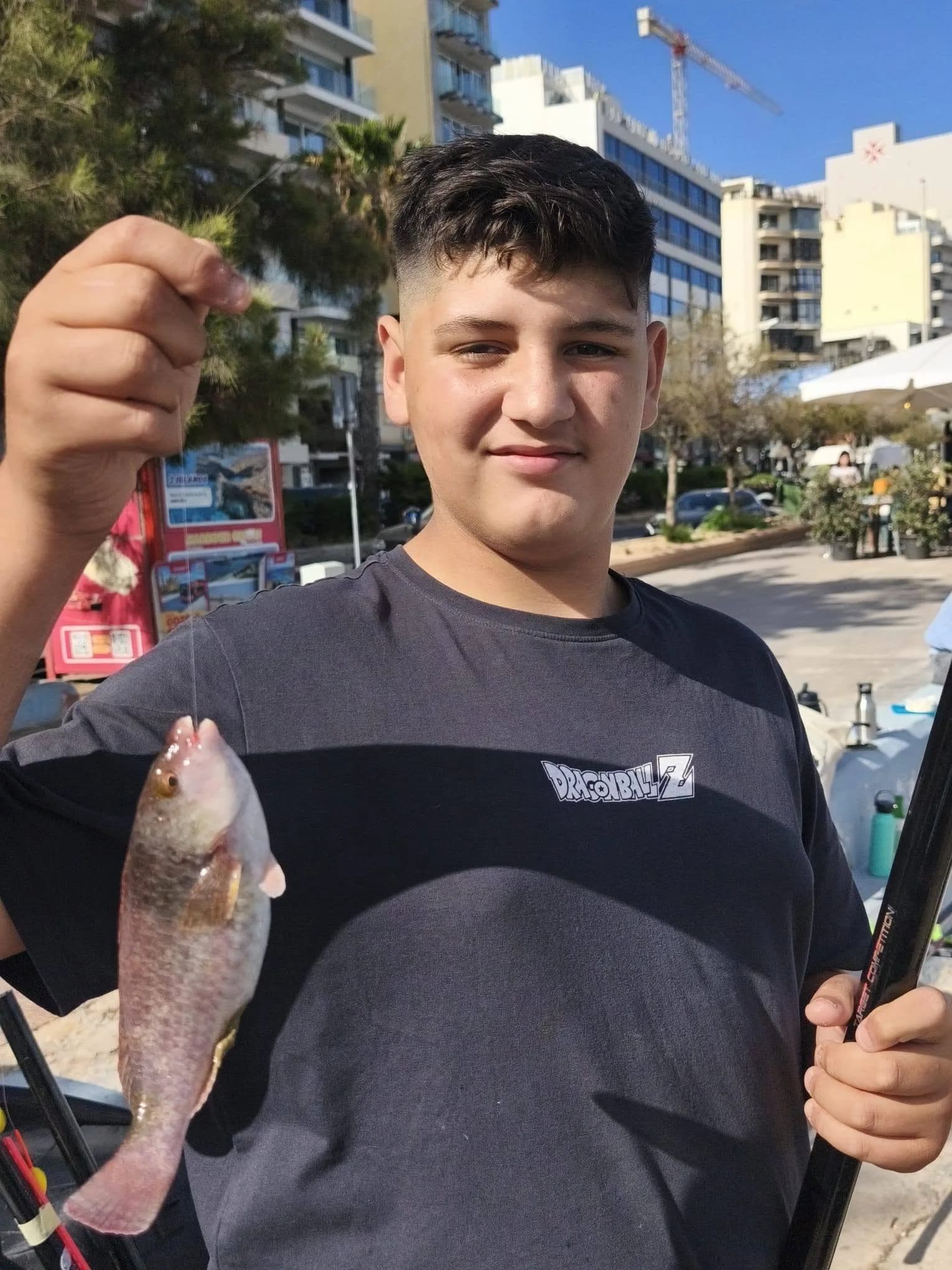 A young angler in a white shirt holding a pole and fish by the sea